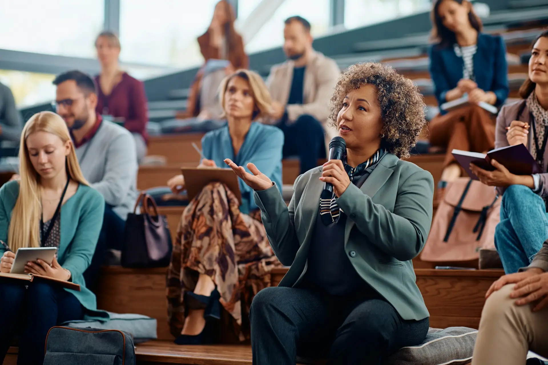 Mature businesswoman using microphone while speaking from audience during a seminar.